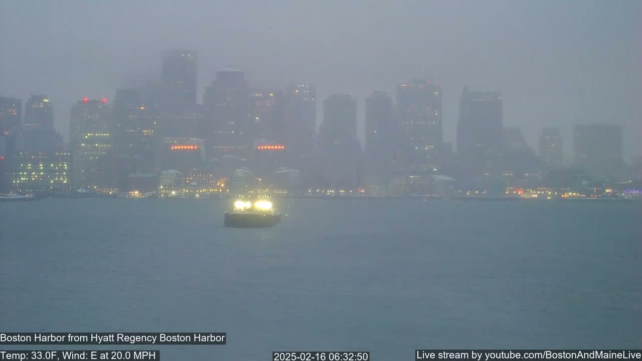 A hazy, foggy cityscape is visible across a body of water, with a single boat illuminated in the foreground, under an overcast sky with an easterly wind.