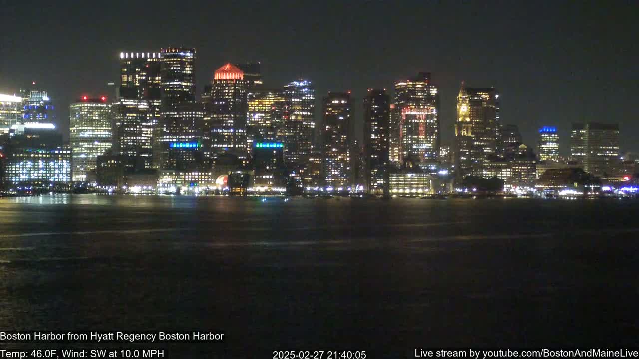 A brightly lit city skyline is seen across a dark body of water at night, with a southwest wind blowing at 10 mph and a temperature of 46 degrees Fahrenheit.