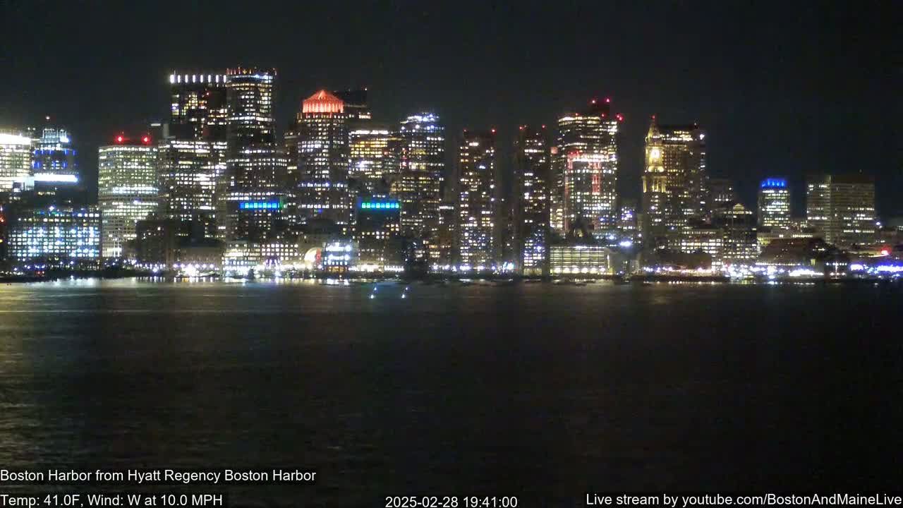 A brightly lit city skyline is seen across a dark body of water at night, with a west wind of 10 mph and a temperature of 41°F.