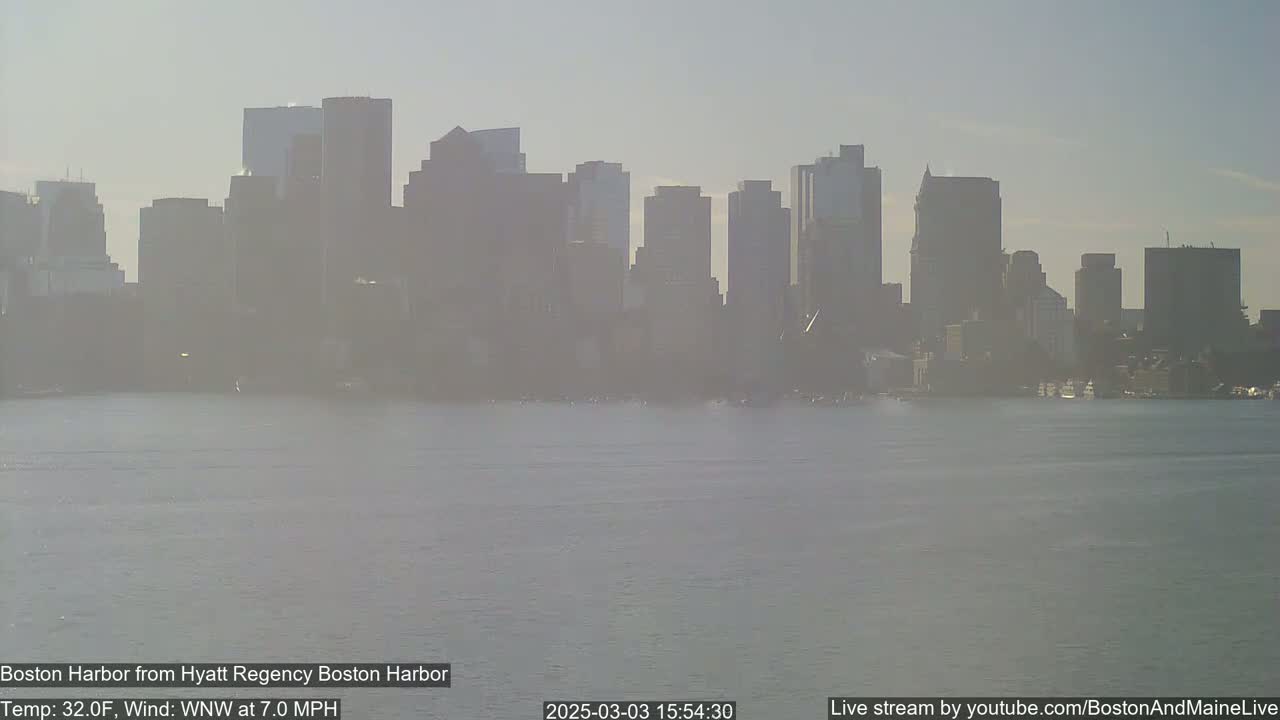 A hazy view of the Boston skyline across calm harbor water on a 32°F day with a 7 mph wind from the west-northwest.
