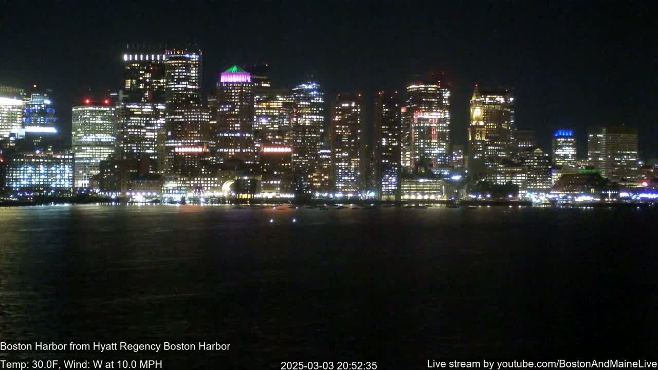 A brightly lit city skyline at night is seen across a dark body of water, with a 30°F temperature and a 10 mph west wind.