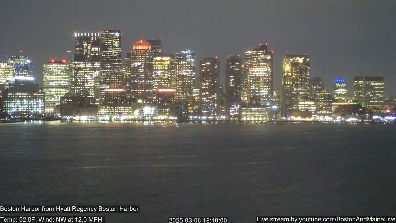 A nighttime view of a city skyline across a body of water, with a northwest wind at 12 mph and a temperature of 52°F.