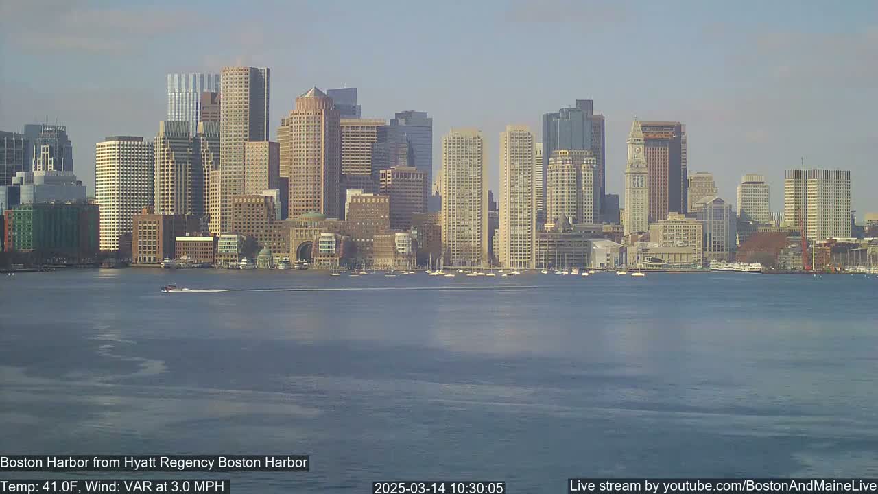 A city skyline of numerous high-rise buildings is seen across a calm body of water on a clear day.