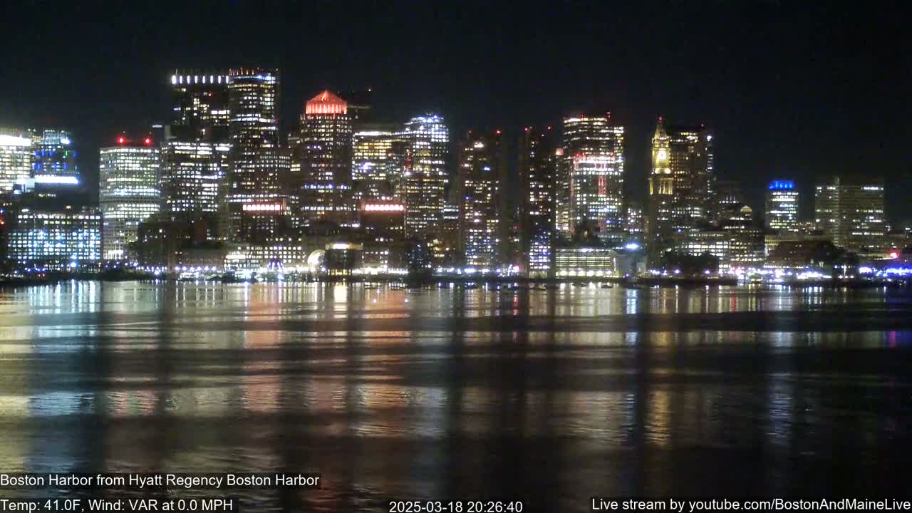 A brightly lit city skyline at night is reflected in calm water.