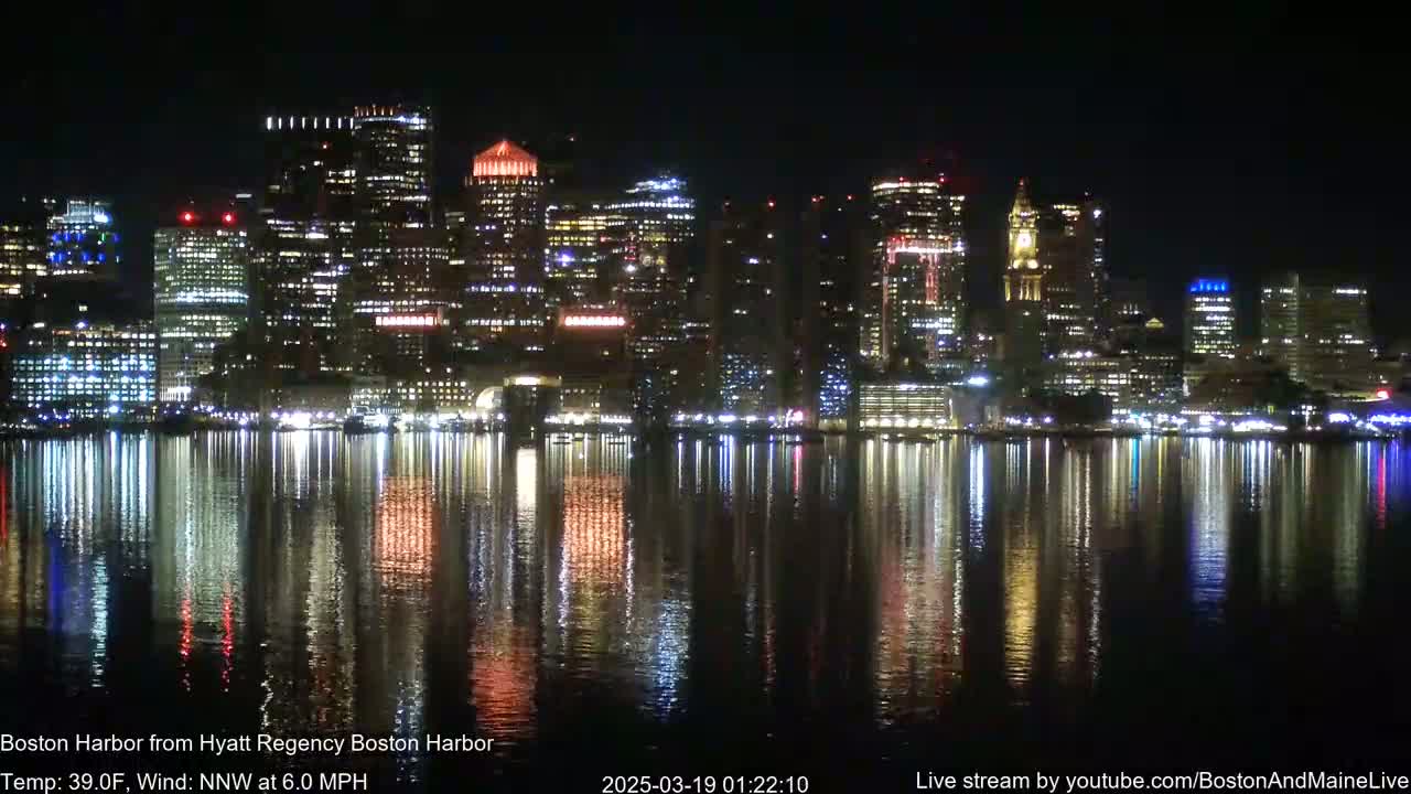 A brightly lit city skyline at night is reflected in a calm body of water.
