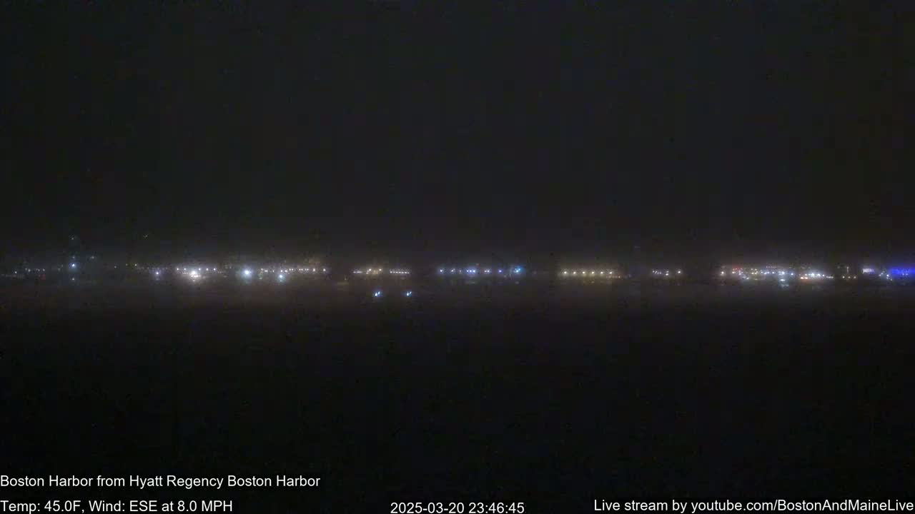 A hazy, dark nighttime view shows a distant line of lights across a flat landscape under an overcast sky.