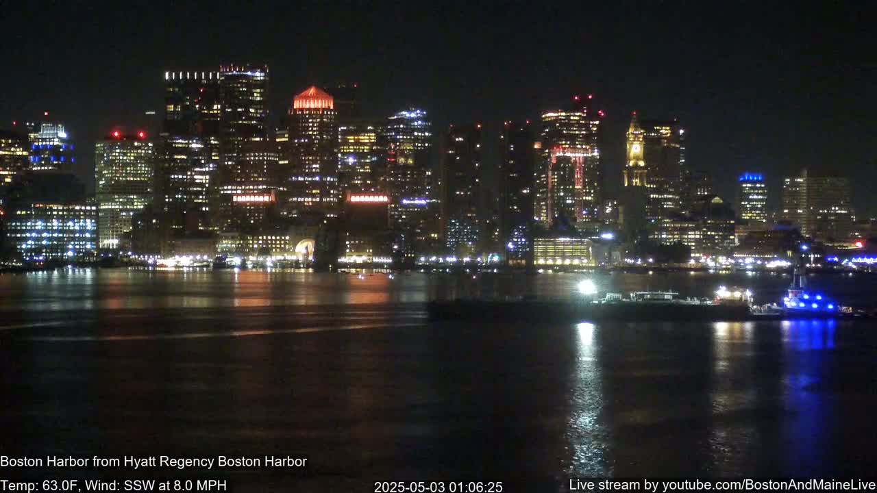 A brightly lit city skyline is reflected in dark water at night, under a clear sky with a slight breeze.