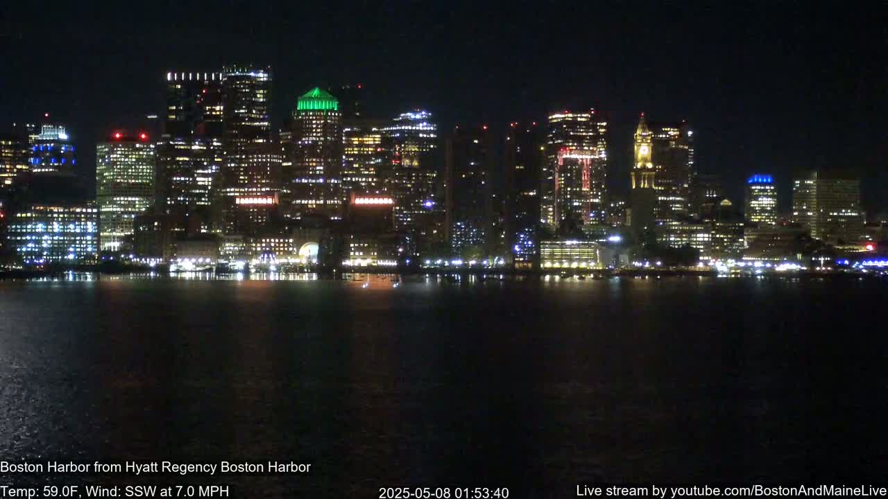 A brightly lit cityscape at night is reflected in dark water under a clear sky.