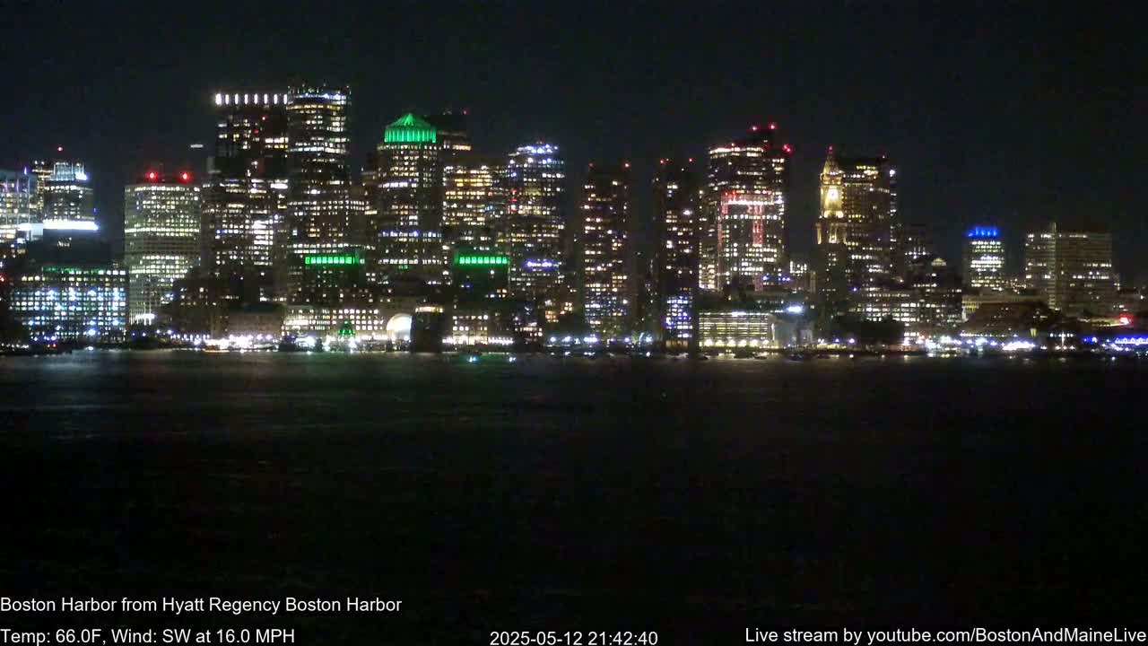 A brightly lit city skyline is seen across a dark body of water at night, with a southwest wind blowing at 16 mph and a temperature of 66°F.