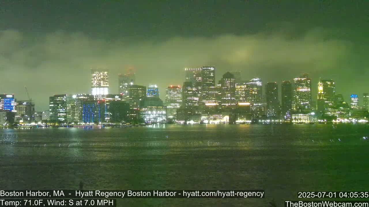 A nighttime view of a city skyline across a body of water under a hazy, foggy sky.