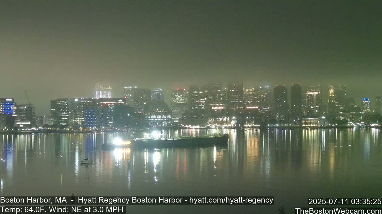 A hazy nighttime view of a city skyline reflected in calm water, with a large ship visible in the foreground.