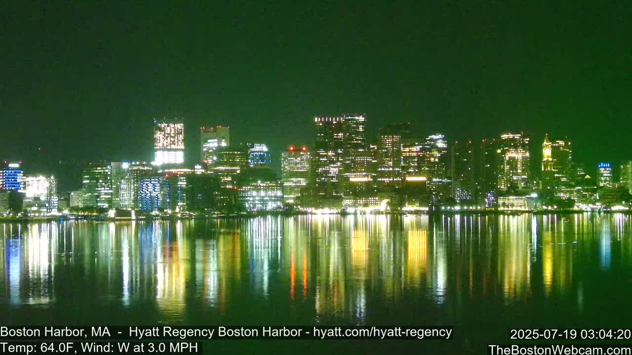 A nighttime cityscape reflects in calm water under a dark green sky.