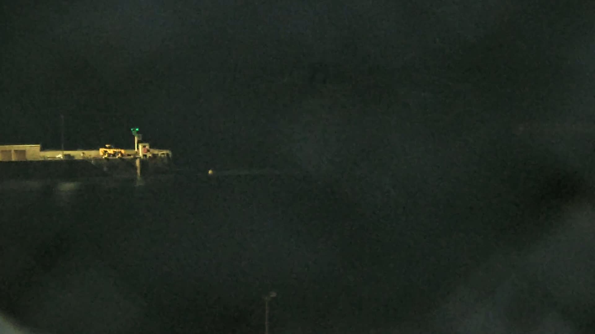 A dimly lit building with a small light on top is visible at night under a dark, overcast sky.
