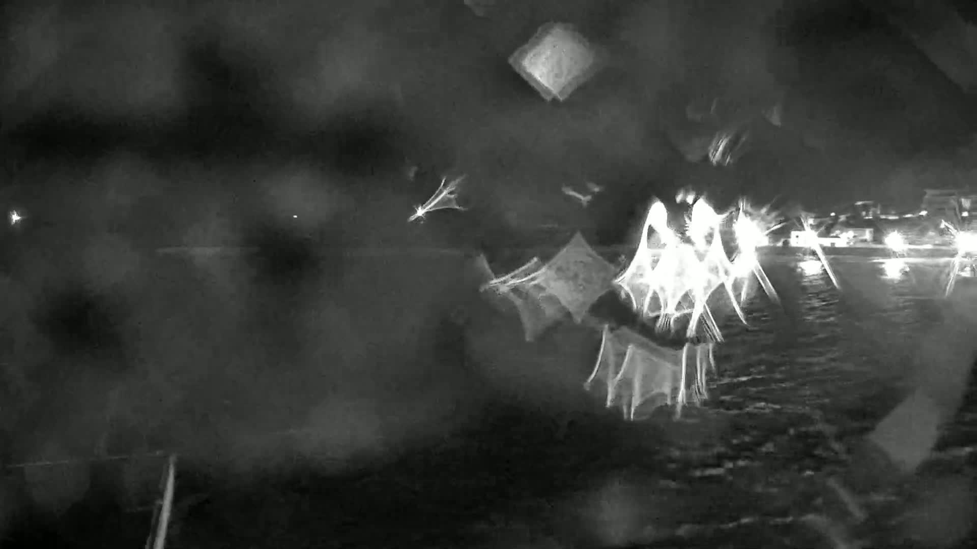 A nighttime, blurry view of water with lights in the distance, possibly from a shore, with rain or moisture obscuring the view.