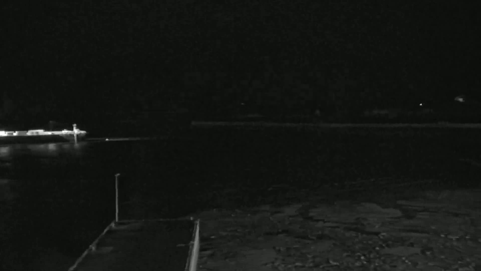 A dark, nighttime scene shows a body of water with a dimly lit vessel and shoreline in the distance.
