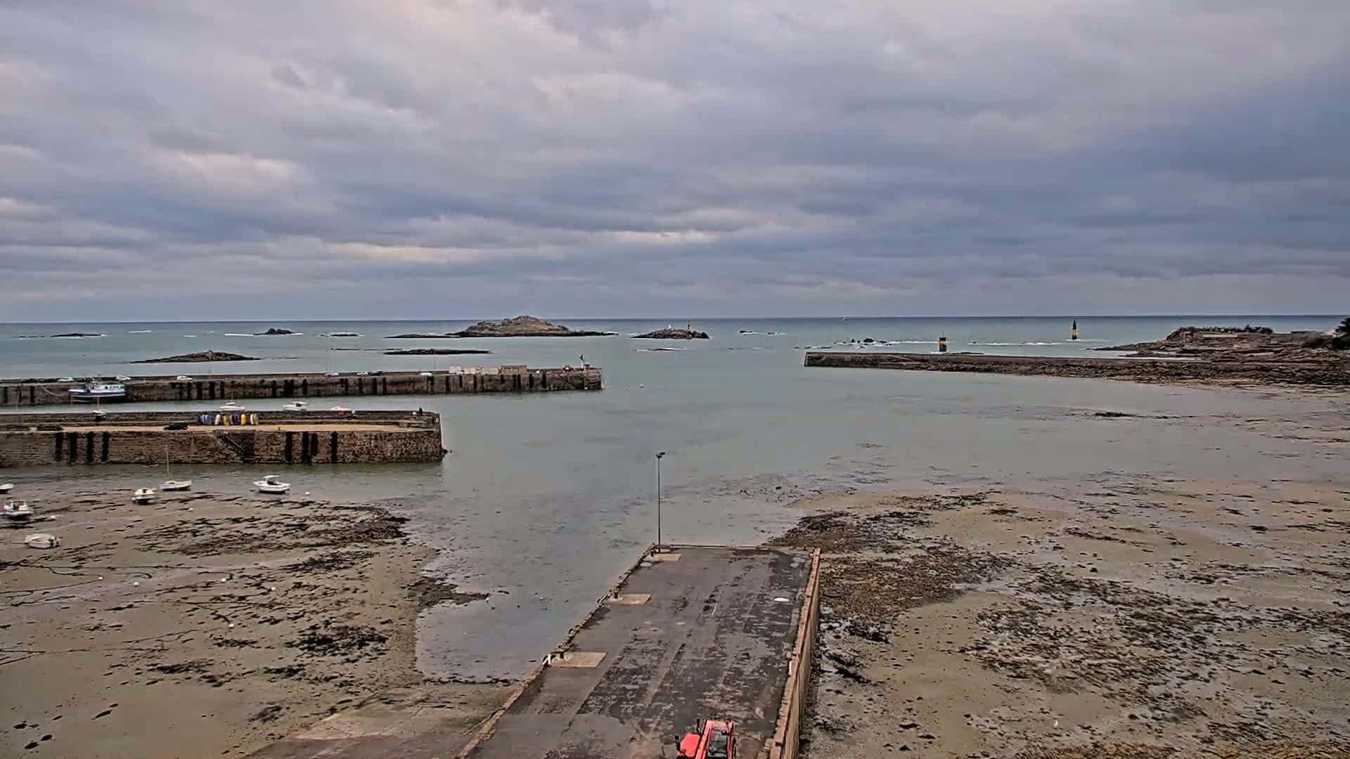 A harbor with several small boats sits on a mostly exposed, sandy seabed under a cloudy sky.