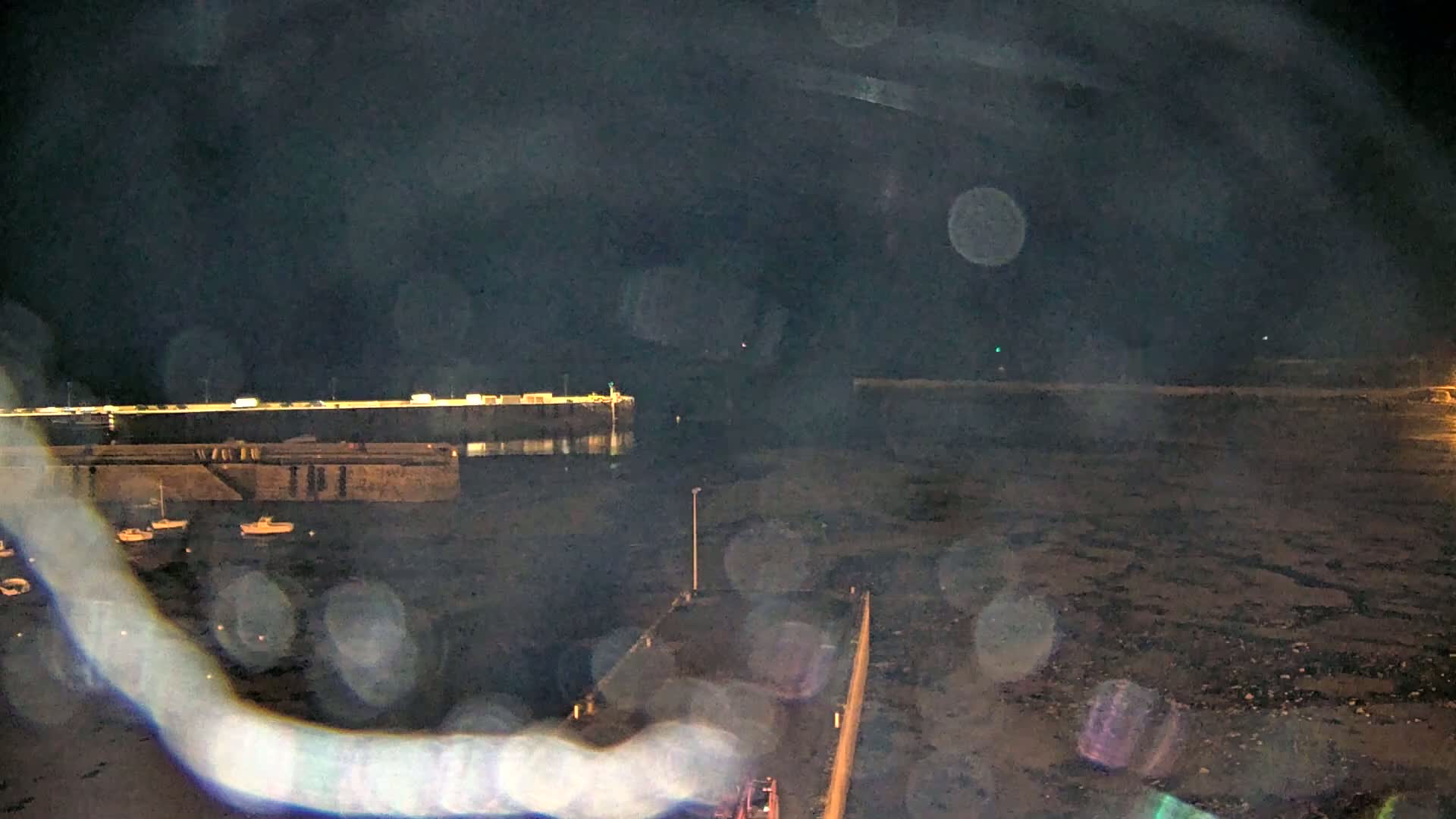 A nighttime view of a harbor with several small boats moored near a pier, under a dark, hazy sky.
