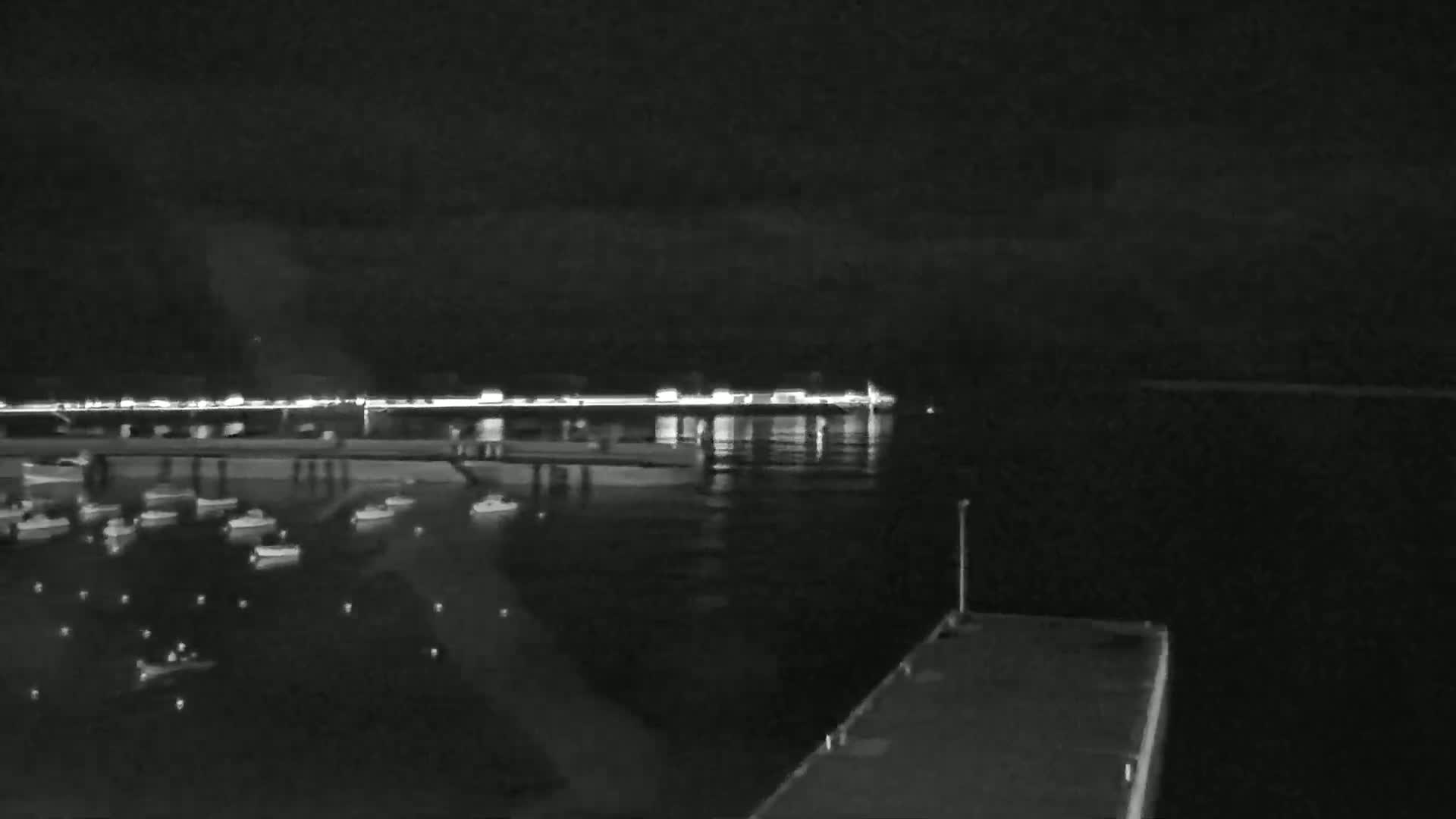 A nighttime view of a harbor shows numerous small boats moored near a brightly lit waterfront.