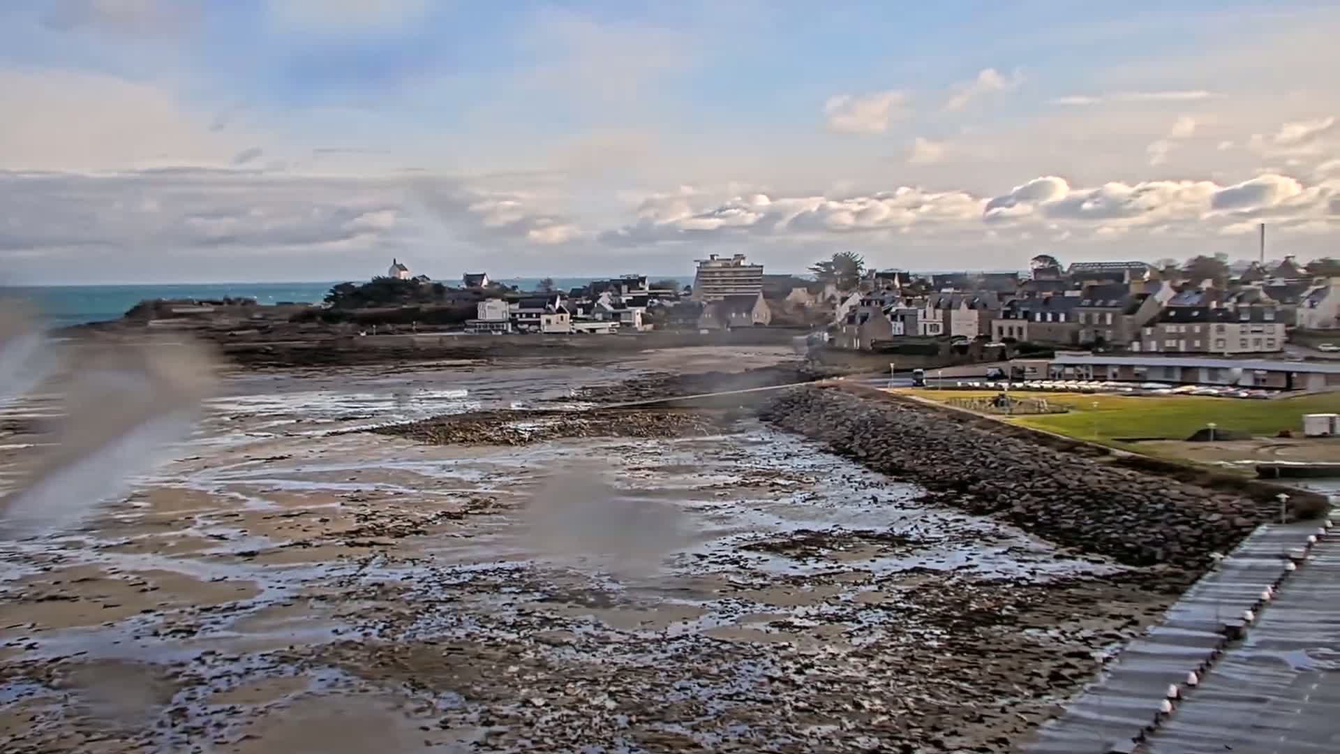 A coastal town is partially visible beyond a wide expanse of exposed mudflats at low tide under a partly cloudy sky.