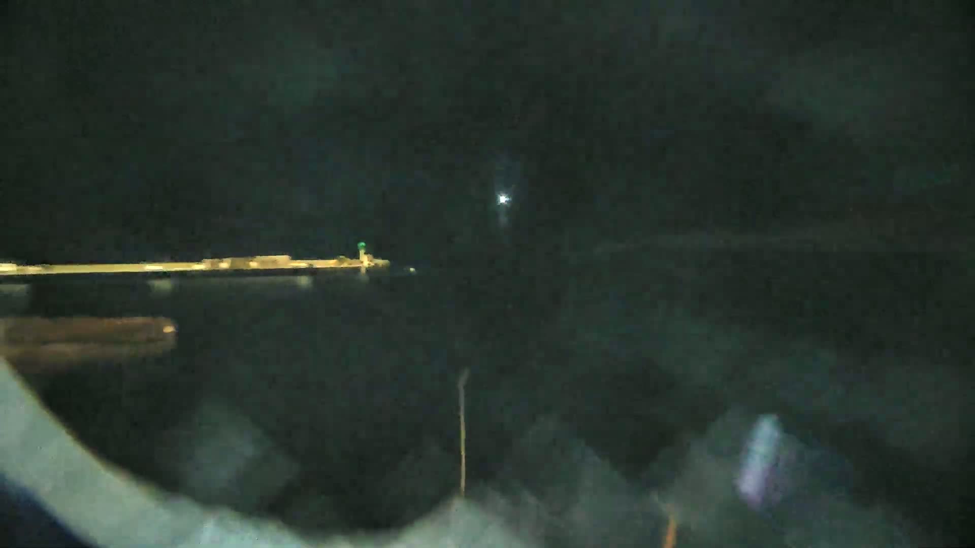 A nighttime view of a dark body of water with a dimly lit pier and a small light on a distant structure.