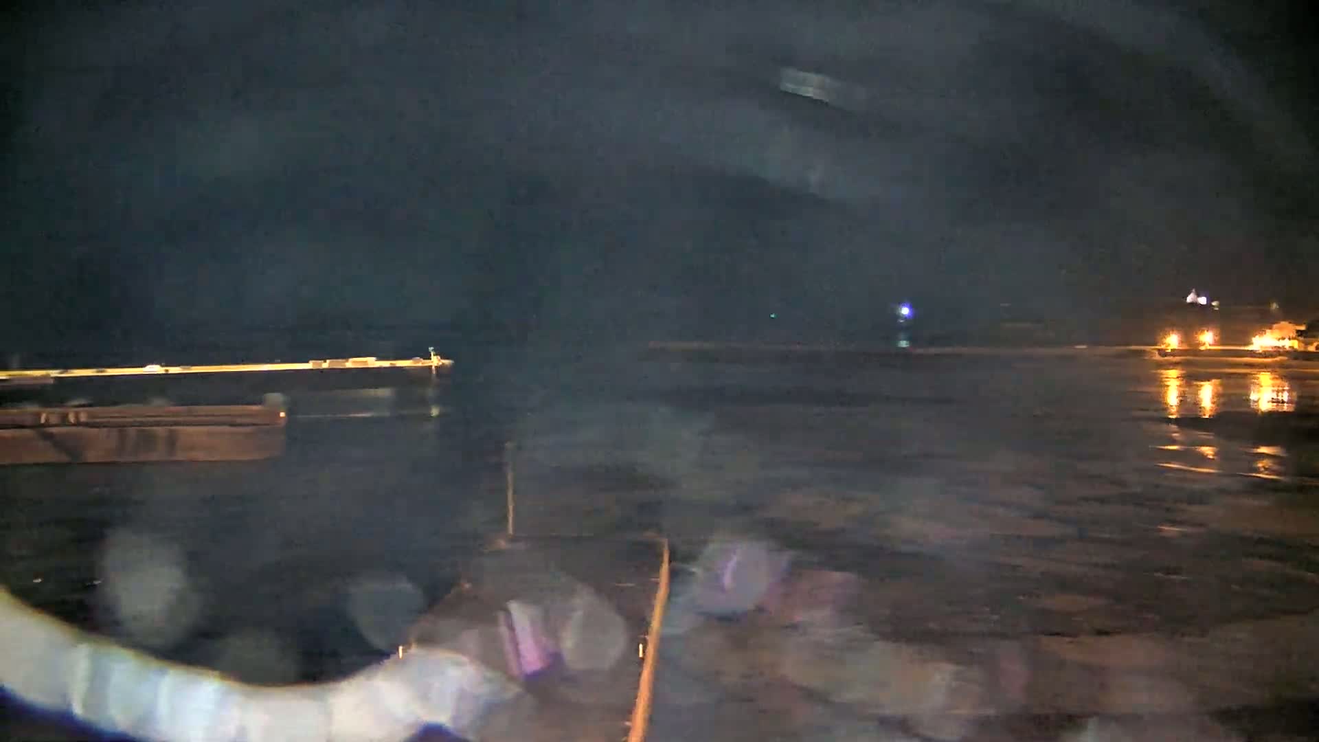 A nighttime view of a calm body of water with a pier and distant lights reflecting on the water's surface.
