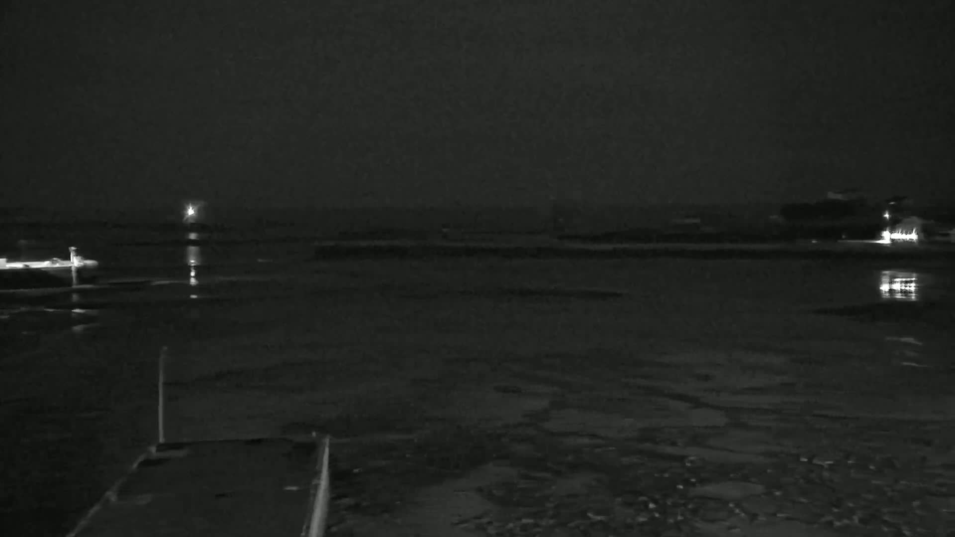 A nighttime, low-light view of a dark body of water with a few lights visible in the distance and a dark structure in the foreground.