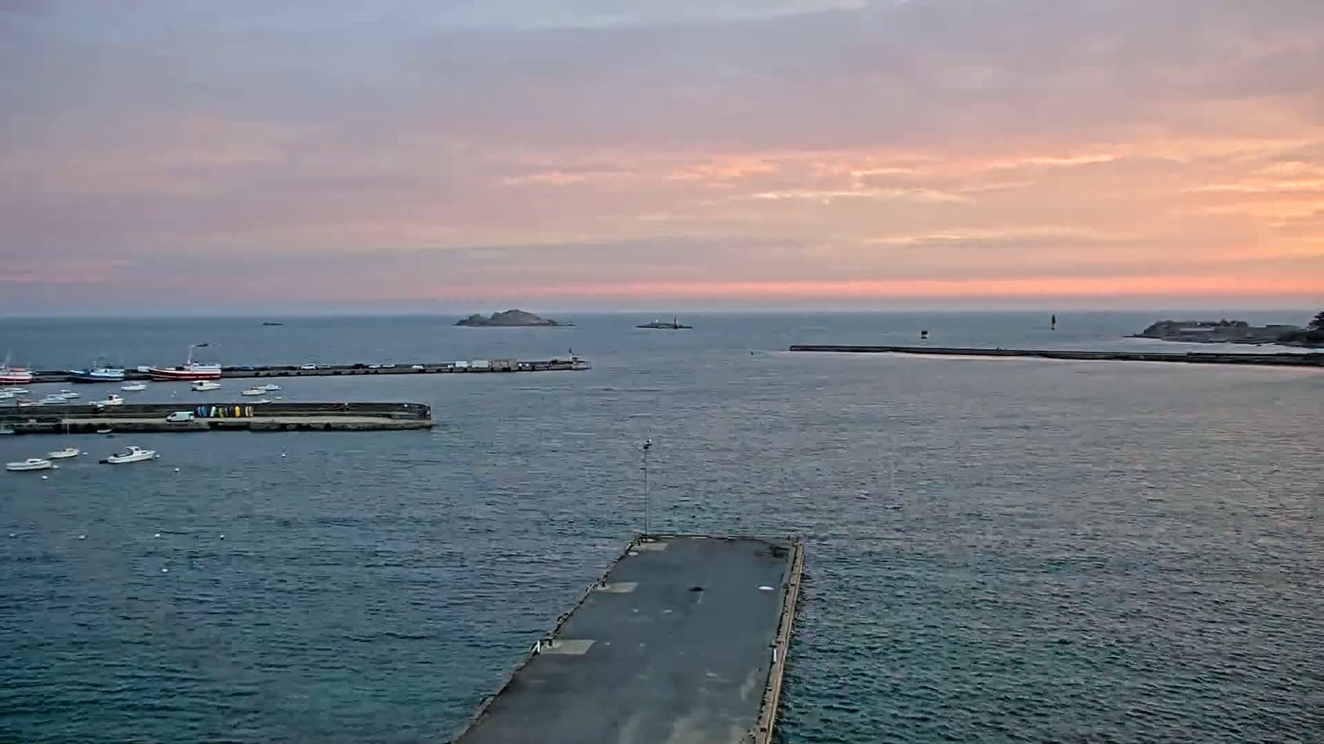 A harbor filled with boats is seen at sunset under a pink and gray sky.