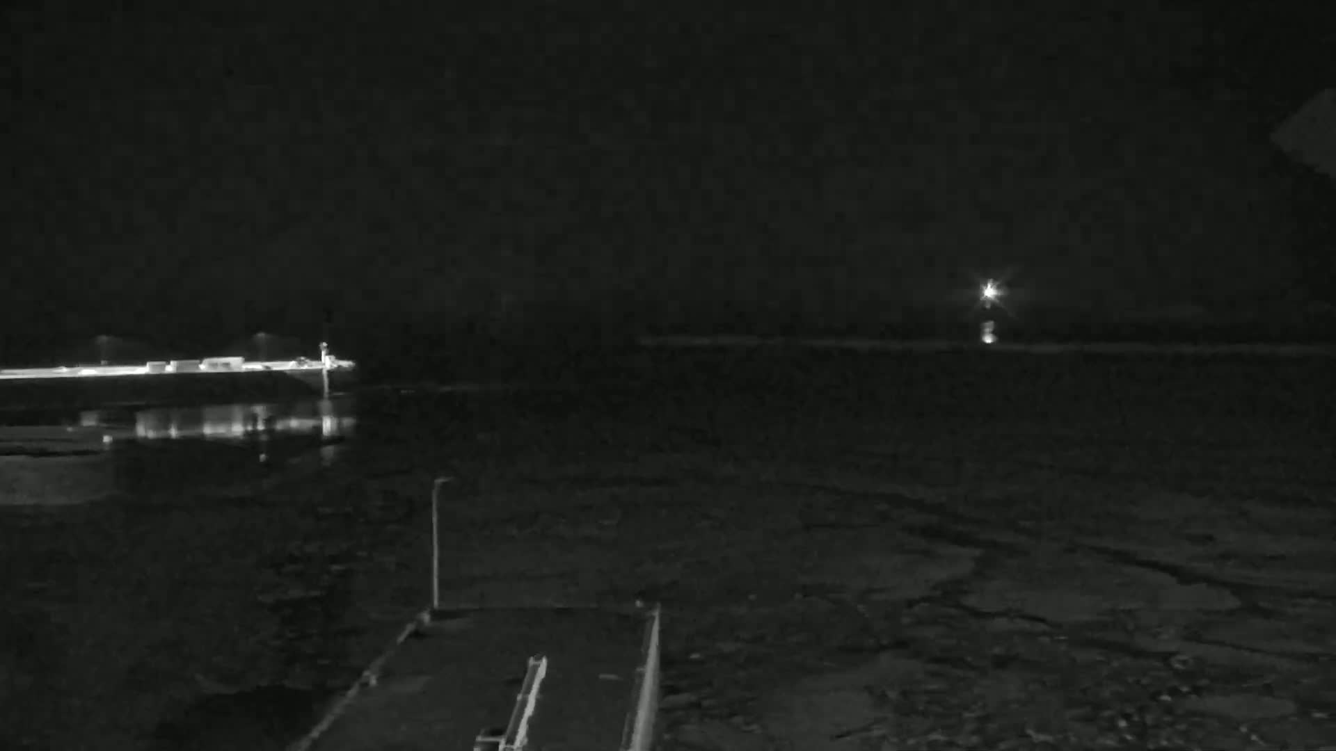 A nighttime view of a dark body of water with a distant light source and a shoreline featuring buildings and a dock.