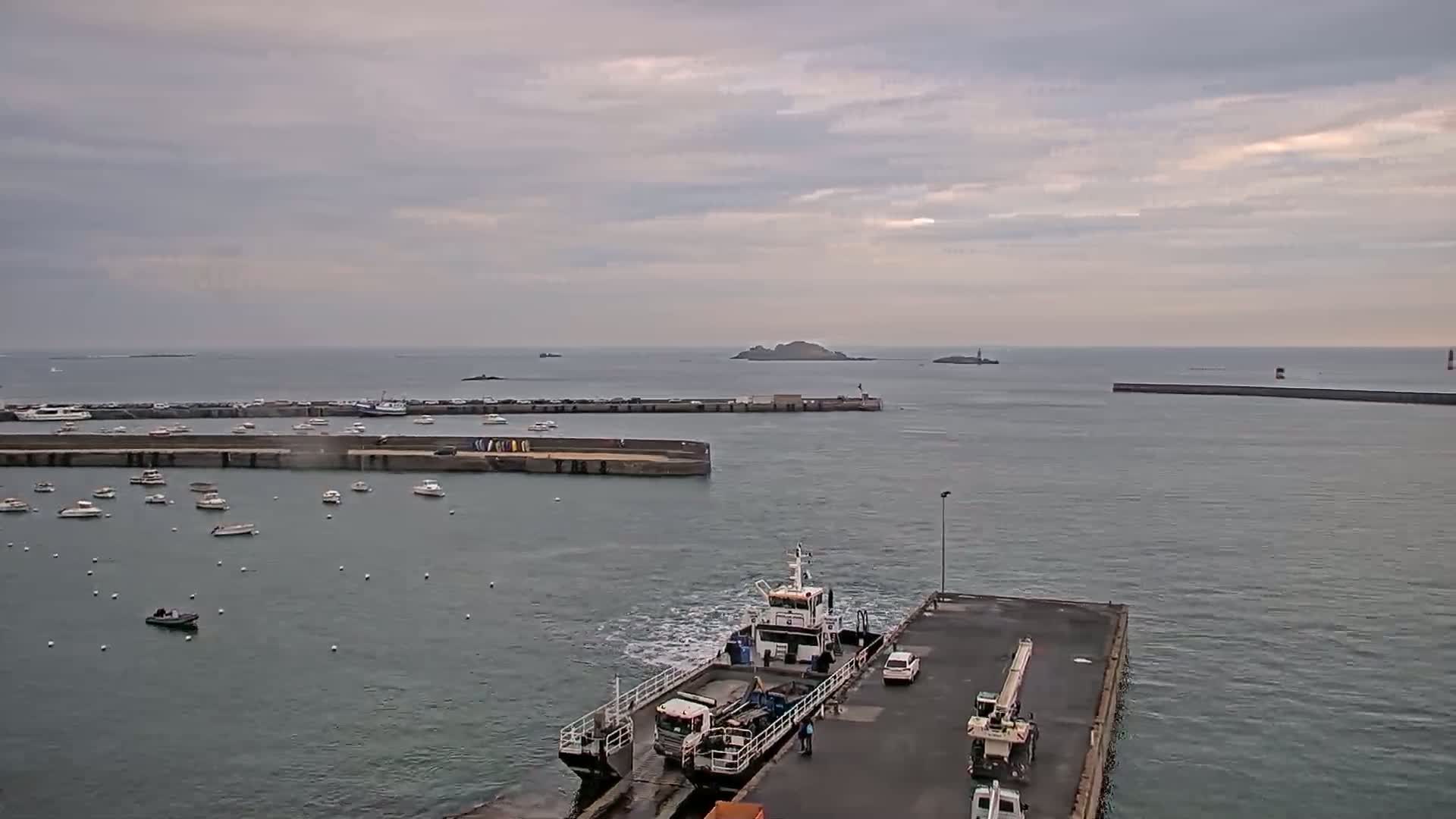 A ferry approaches a dock in a harbor filled with numerous small boats under an overcast sky.