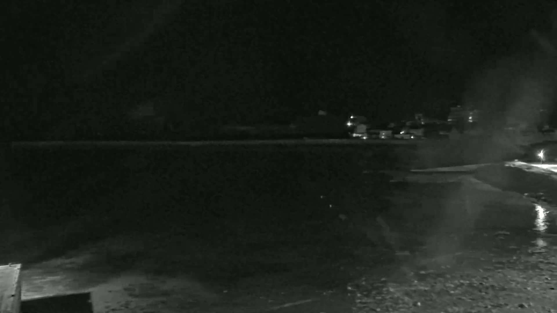 A nighttime, low-light view of a dark body of water reflecting a dimly lit shoreline with buildings in the distance.