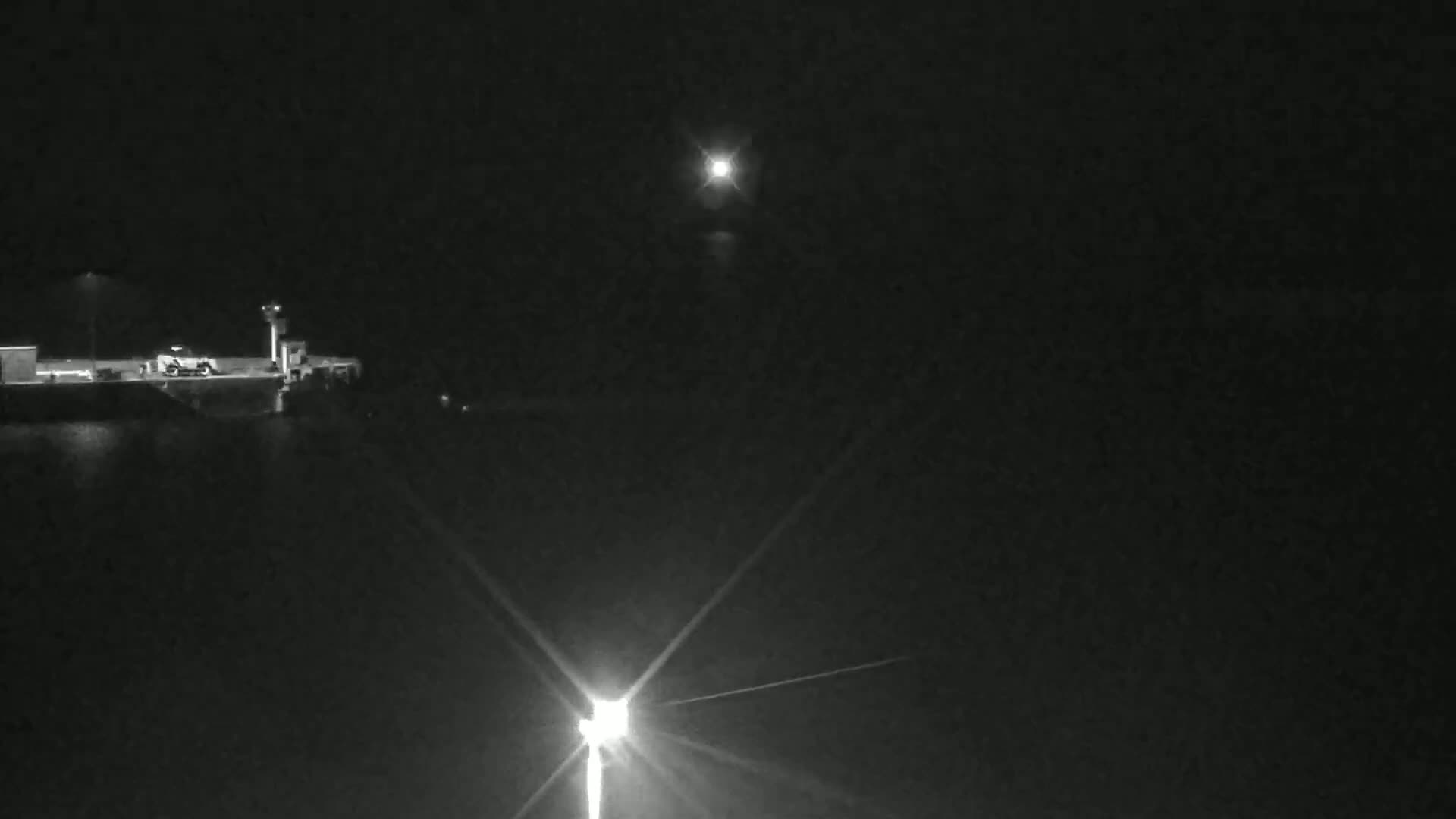 A nighttime view of a dark body of water with a distant bright light and a closer, brighter light near a dock.