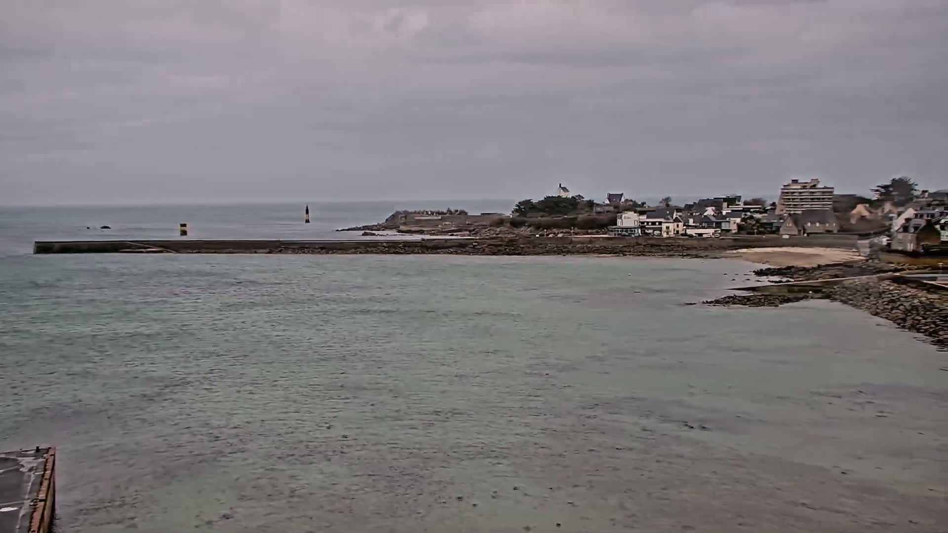 A calm body of water stretches out to a shoreline with a small town under an overcast sky.