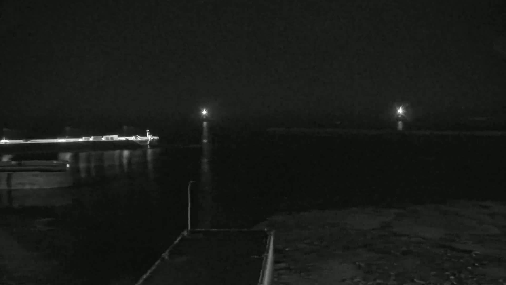 A dark, nighttime view of a calm body of water with lights in the distance on either side, and a dark structure in the foreground.