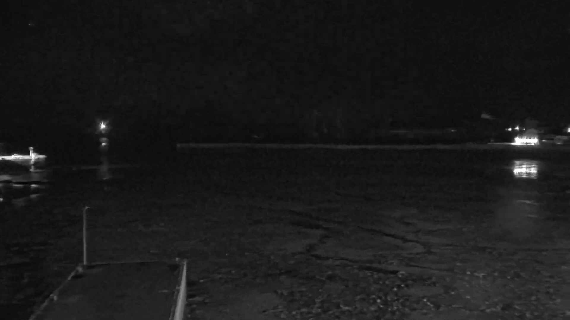 A nighttime view of a dark body of water with patches of ice, faintly lit by distant lights on the shore.