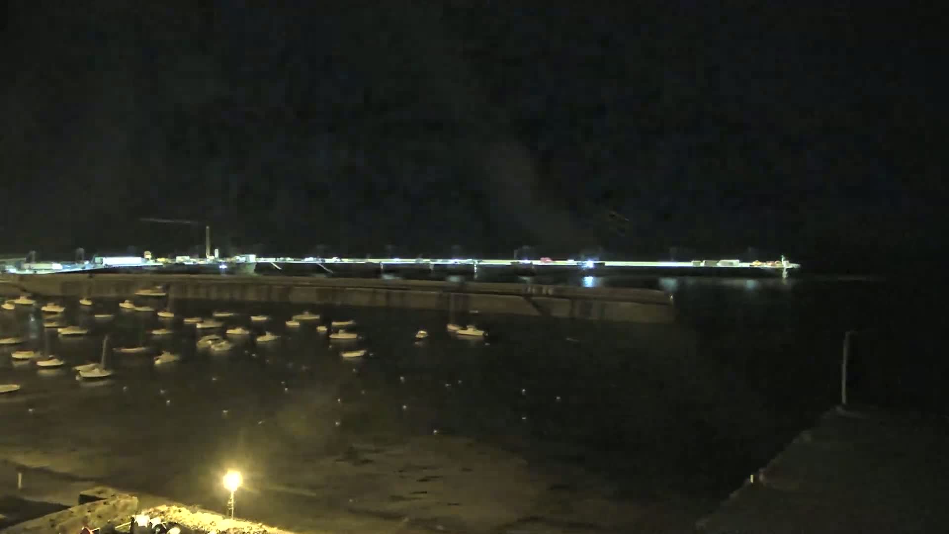 A nighttime view of a harbor filled with numerous small boats, situated below a long, dimly lit waterfront area.