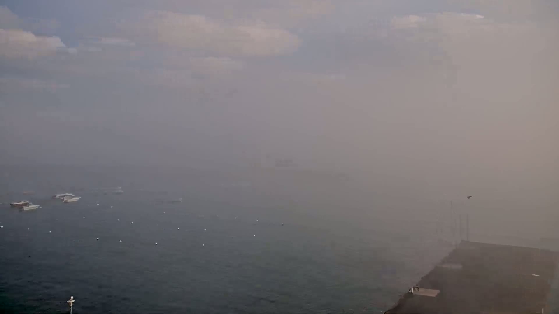 A foggy harbor scene shows several small boats on the water, a pier in the lower right, and a hazy, indistinct background.
