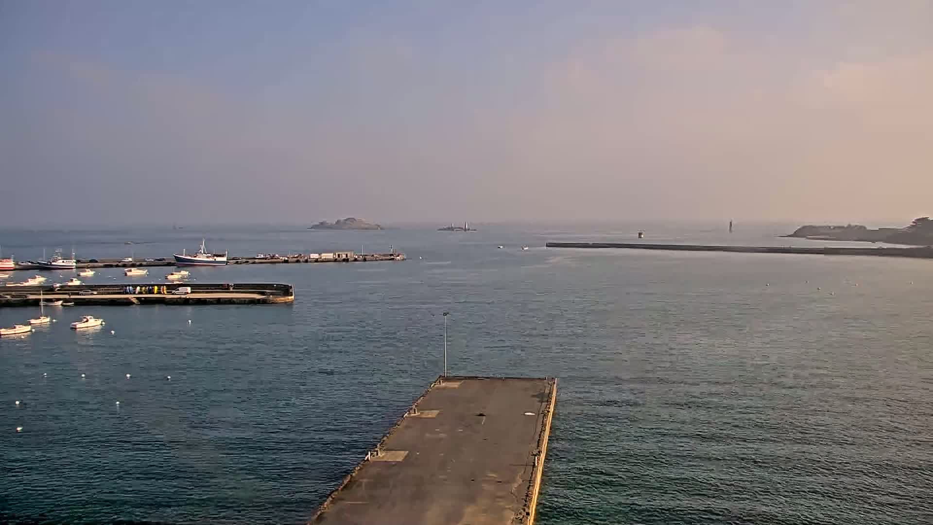 A harbor filled with small boats and a few larger vessels is visible under hazy conditions, with distant islands and landmasses appearing on the horizon.