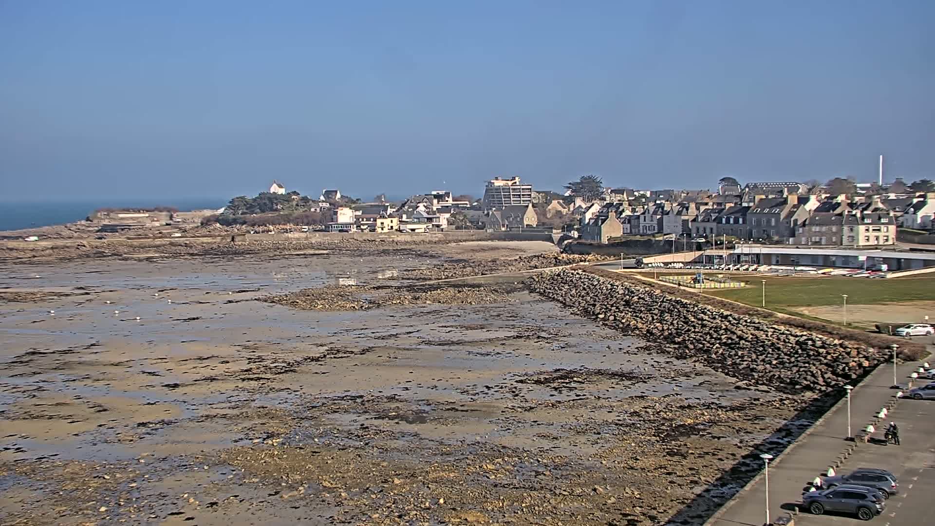 A low-tide, rocky beach stretches out before a coastal town under a clear, sunny sky.