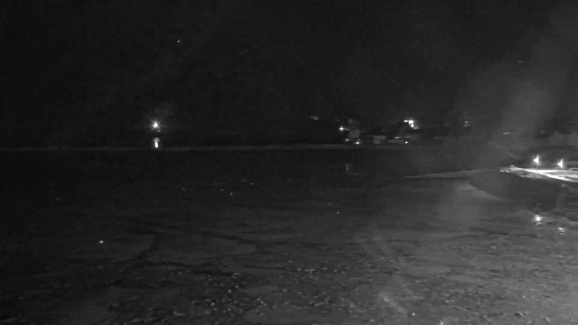 A nighttime view of a dark, icy body of water with faint lights visible in the distance.