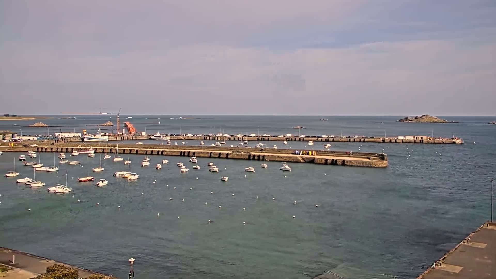 A harbor filled with numerous small boats is enclosed by a stone wall under a partly cloudy sky.