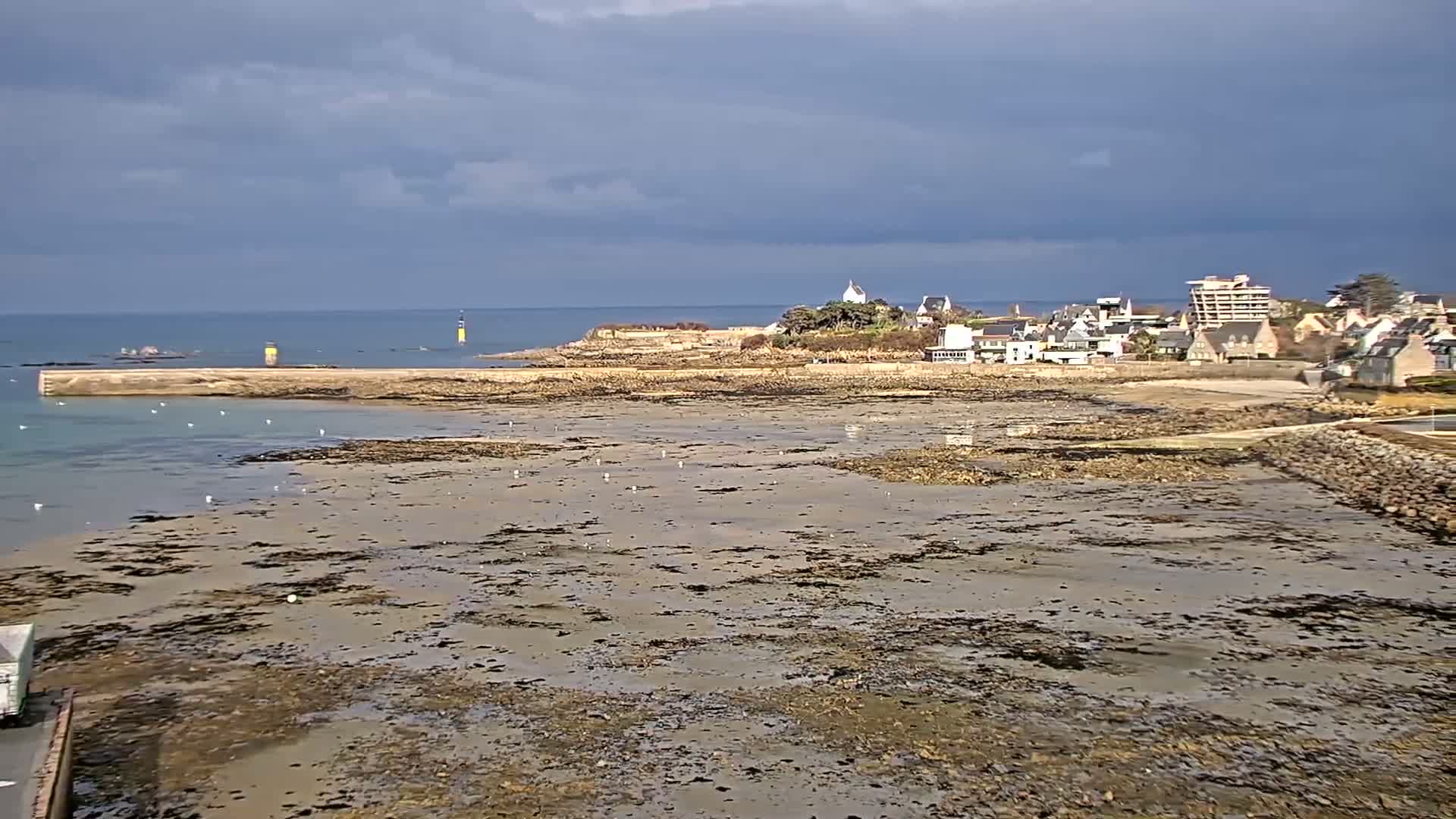 A coastal town is visible across a wide expanse of exposed, muddy tidal flats under a cloudy sky.