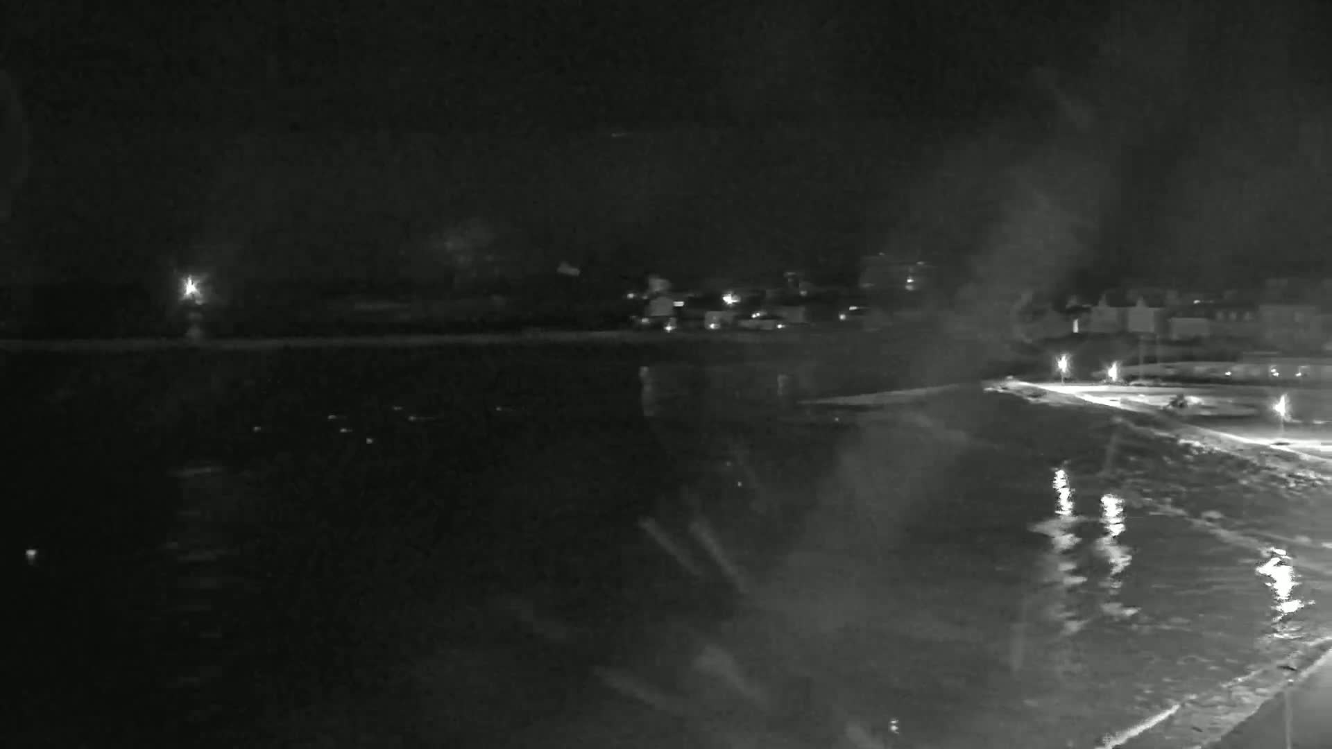 A nighttime, low-light view of a dark body of water with a dimly lit shoreline and buildings in the distance.