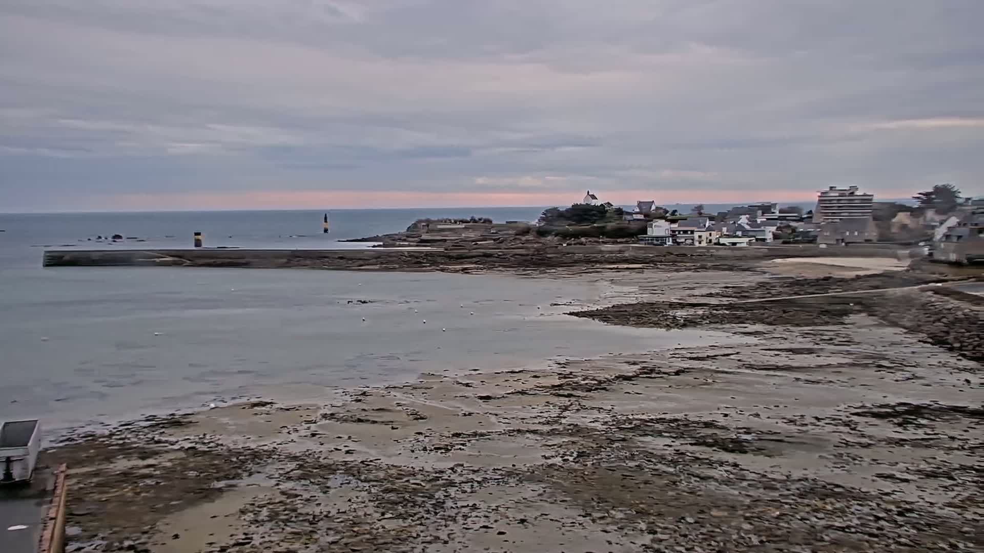 A coastal town is visible across a calm bay at low tide under an overcast sky.
