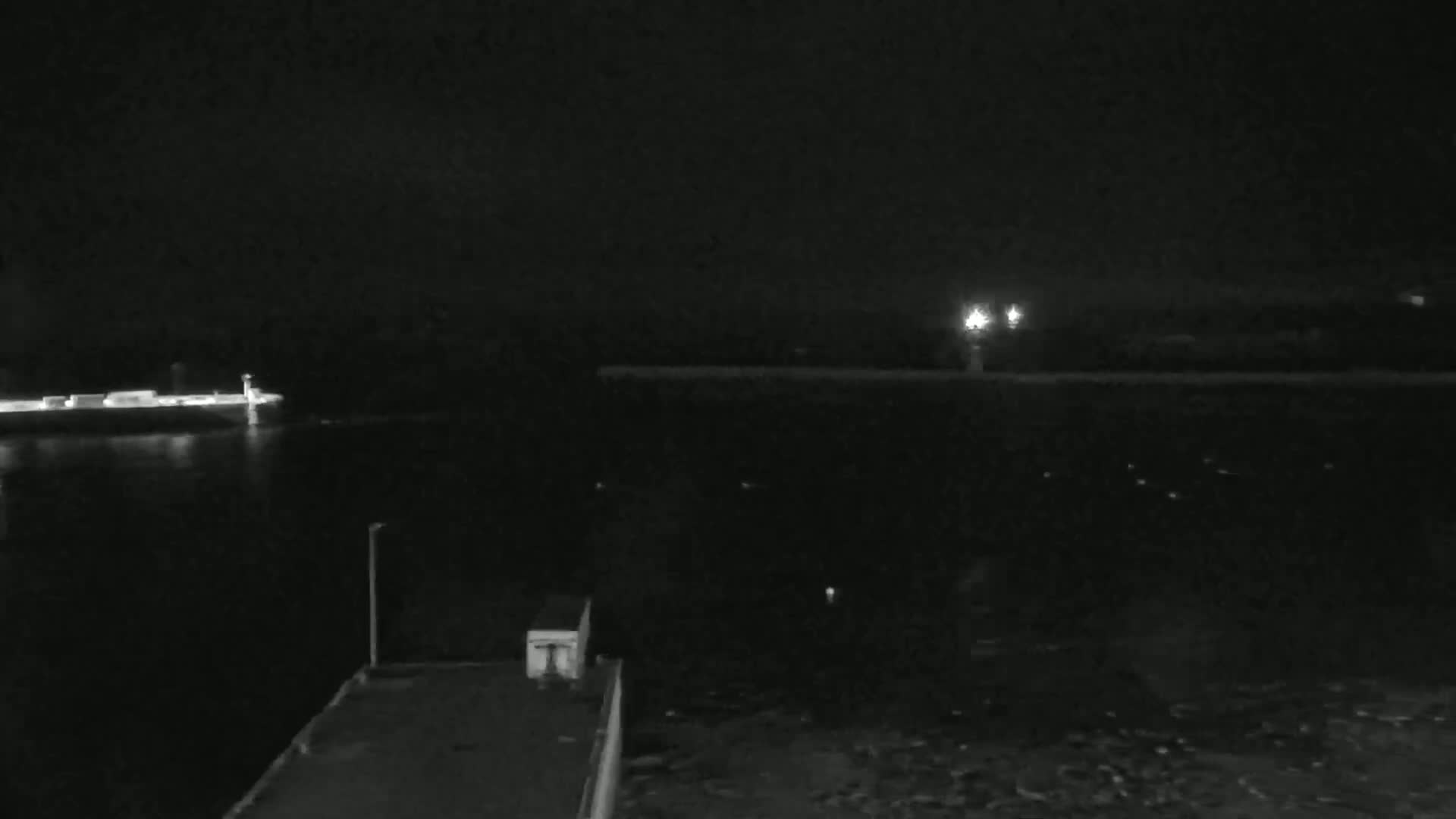 A nighttime view of a dark body of water with a ship and a lit-up pier in the distance.
