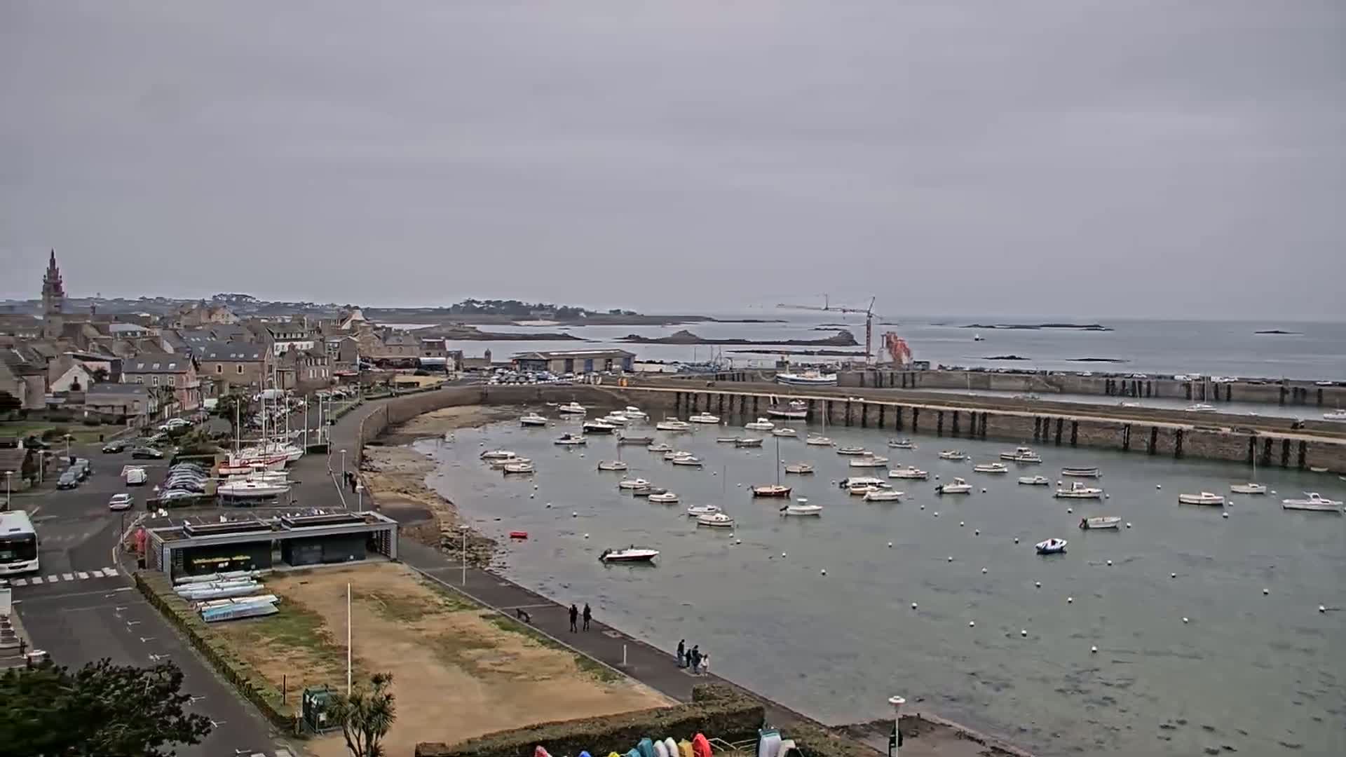 A coastal town with a harbor full of boats is visible under an overcast sky.