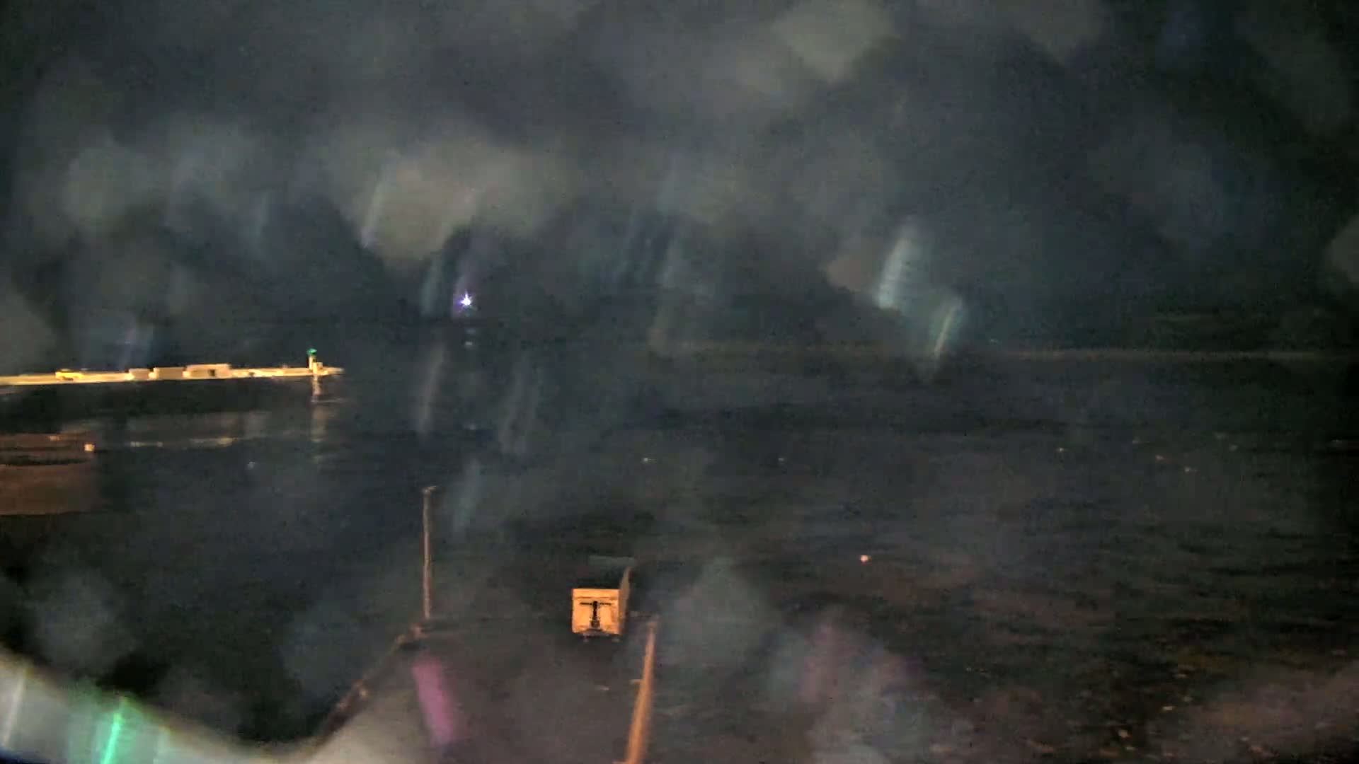 A nighttime, blurry view of a dark body of water with a distant structure and light, seen through a distorted lens.