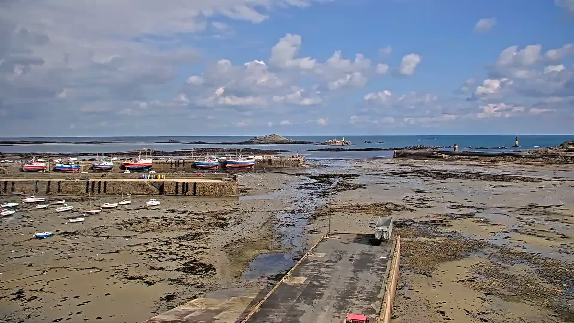 A harbor with numerous boats docked, some sitting on exposed mudflats at low tide, under a partly cloudy sky.