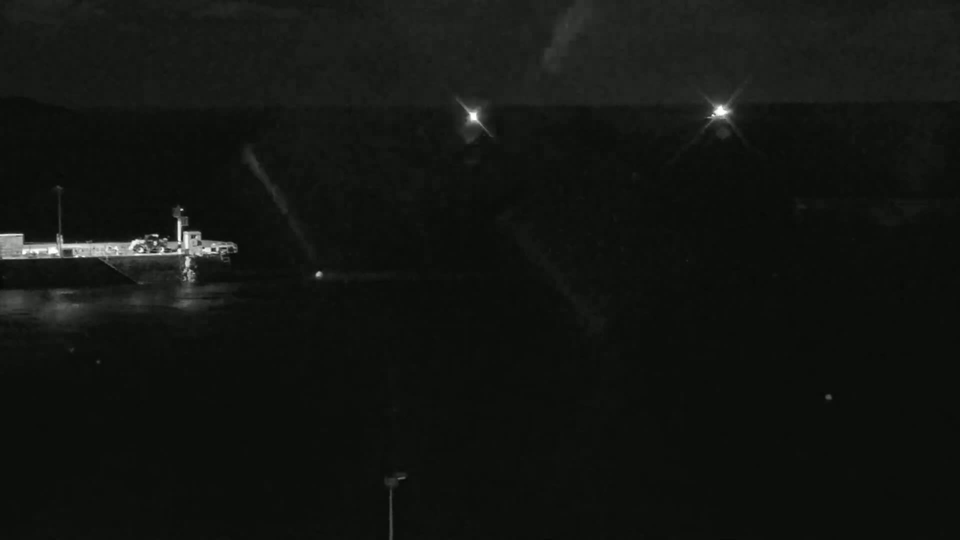 A barge is docked at night near two distant lights under a dark, possibly cloudy sky.