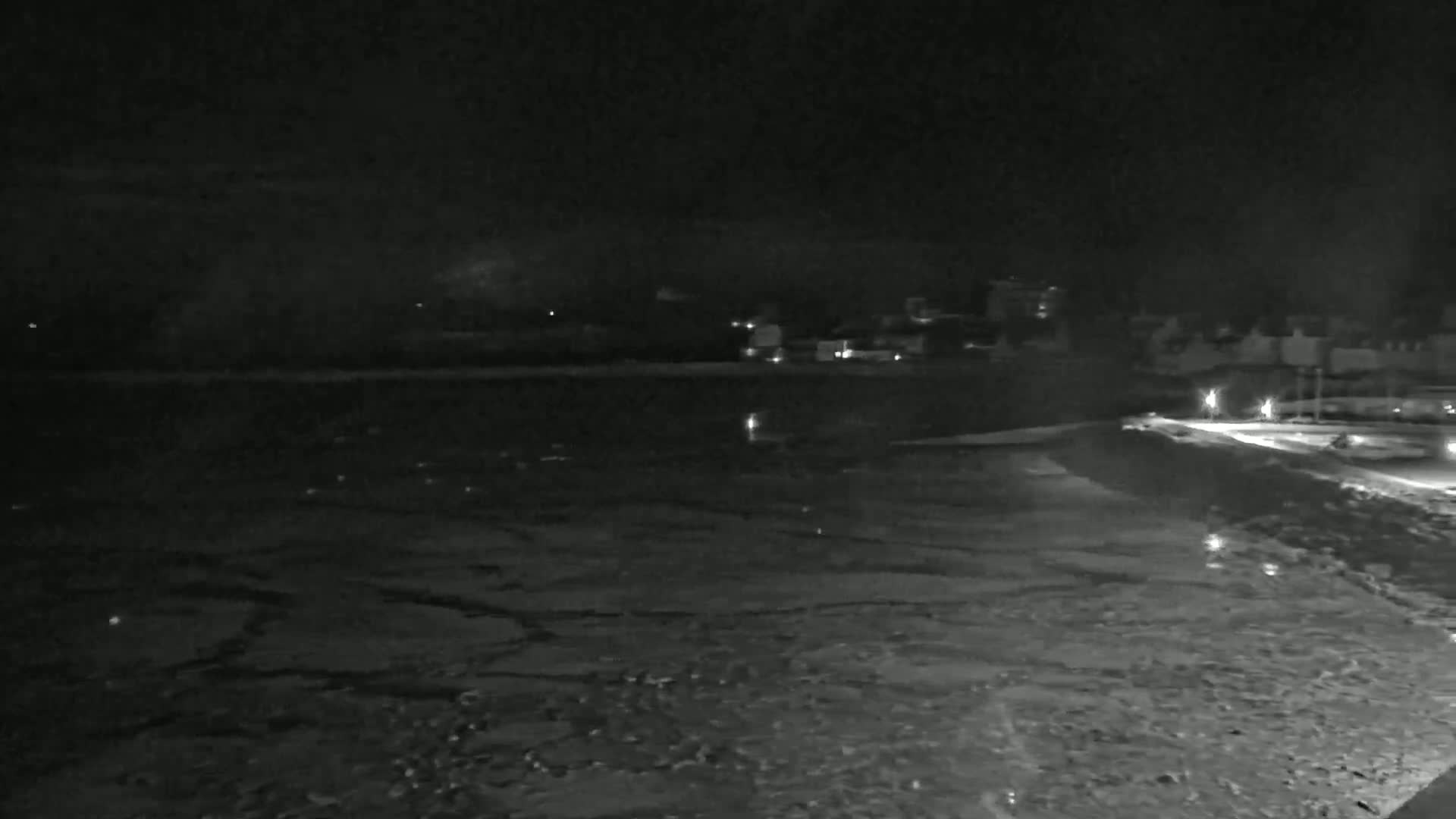 A dark, nighttime view of a snow-covered waterfront with dimly lit buildings in the distance.