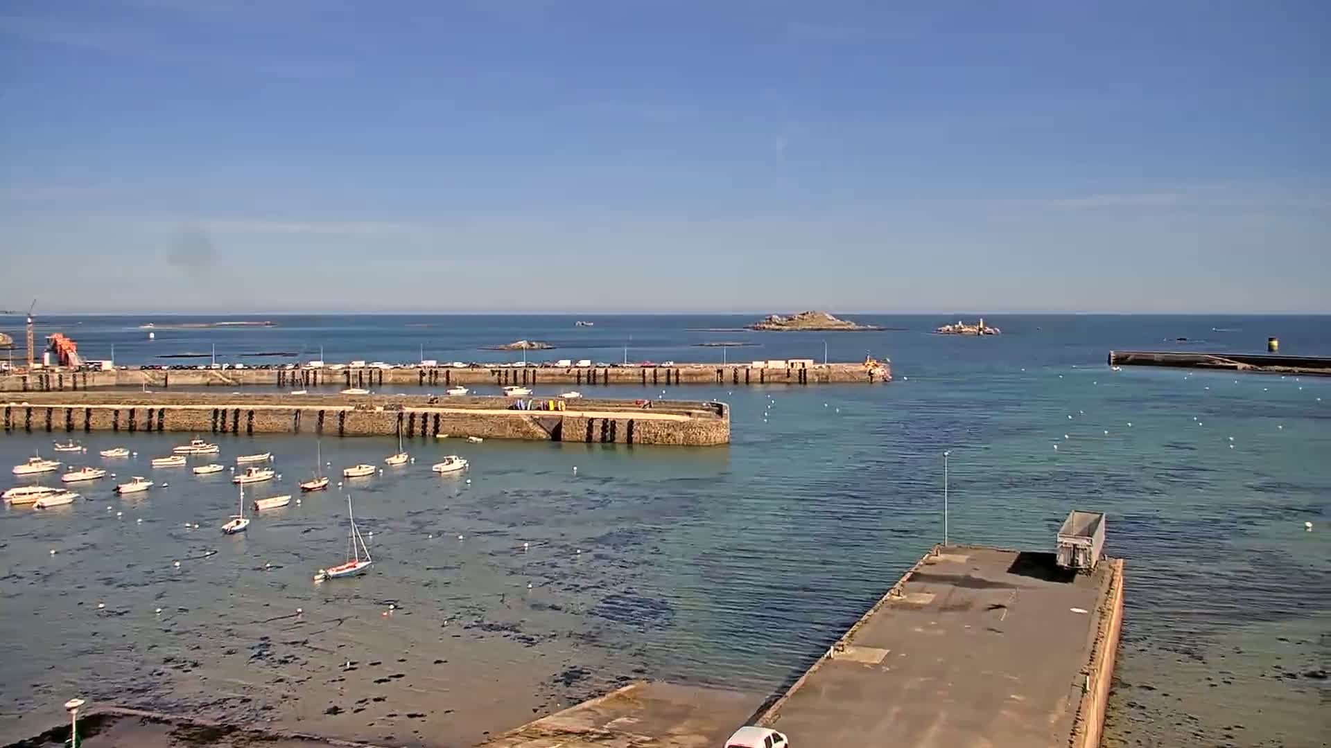 A harbor filled with small boats on a sunny day, with a small island visible in the distance.